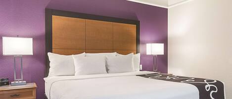 A hotel room with a large bed, two bedside lamps, a wooden headboard, and purple walls.