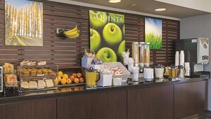 A breakfast buffet with various food items and a large poster of apples.