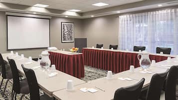 Un salón de conferencias con una larga mesa, sillas, una pantalla de proyector y un amplio ventanal con cortinas translúcidas.