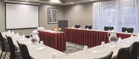 Un salón de conferencias con una larga mesa, sillas, una pantalla de proyector y un amplio ventanal con cortinas translúcidas.