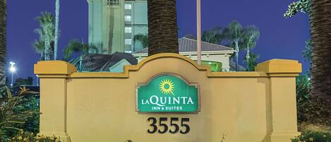 Señal de hotel con el nombre "La Quinta Inn & Suites" y el número "3555" sobre un fondo de cielo nocturno.
