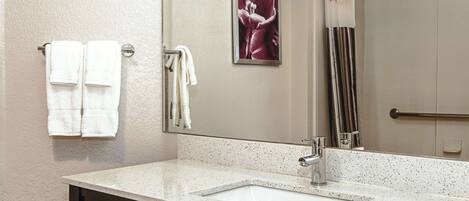 A bathroom with a white speckled countertop, a mirror, and two towels hanging on a towel rack.