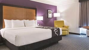 A hotel room with a large bed, a yellow armchair, and a framed picture on the wall.