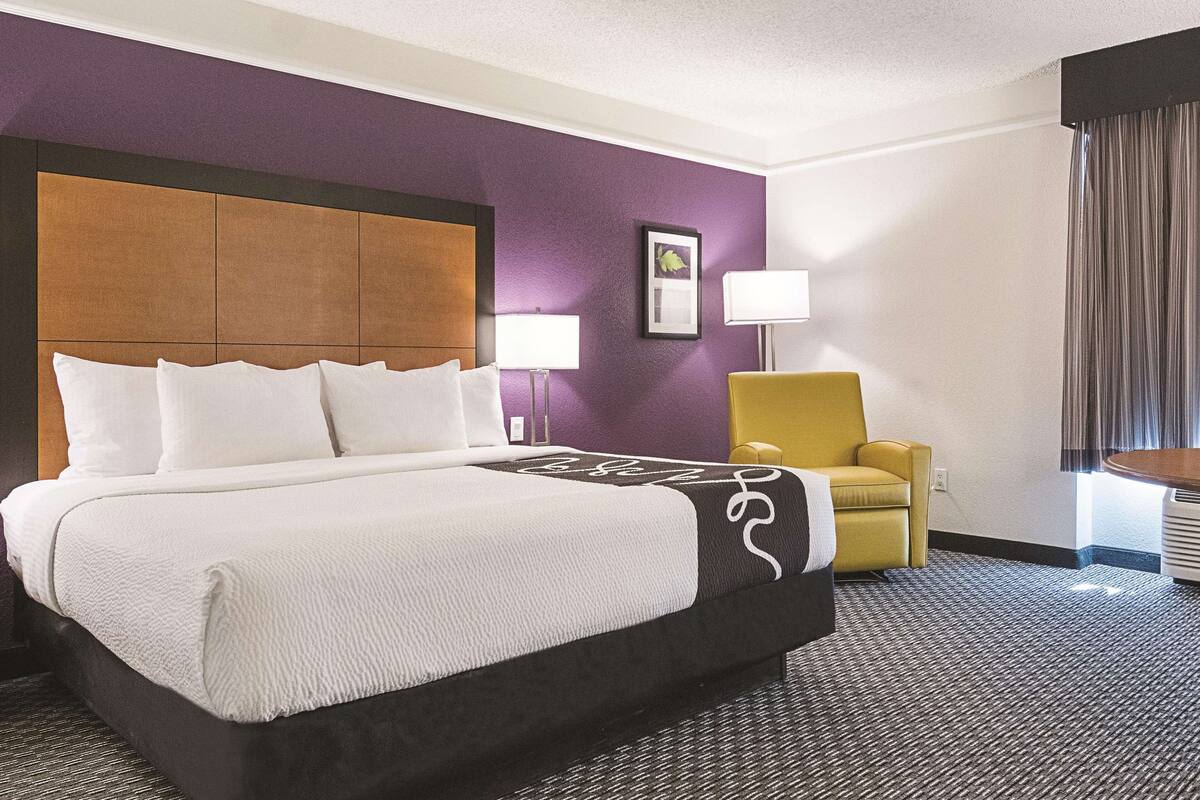 Hotellihuone, jossa on suuri sänky, keltainen nojatuoli ja seinällä oleva kehystetty taulu.