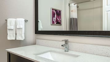 A bathroom with a white sink, a large mirror, and two white towels hanging on a towel rack.