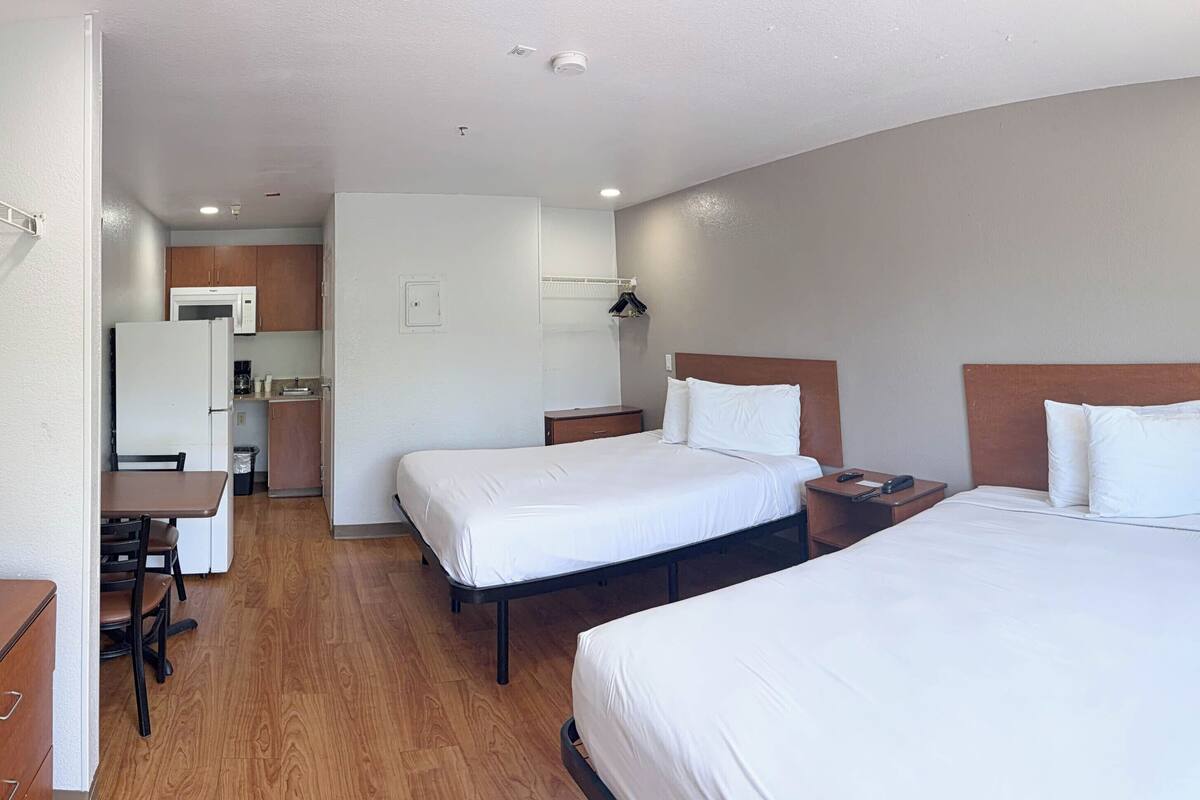 Ein Hotelzimmer mit zwei Betten, einem Schreibtisch, einer Mikrowelle und einer kleinen Küchenzeile.
