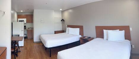 A hotel room with two beds, a desk, a microwave, and a small kitchenette.