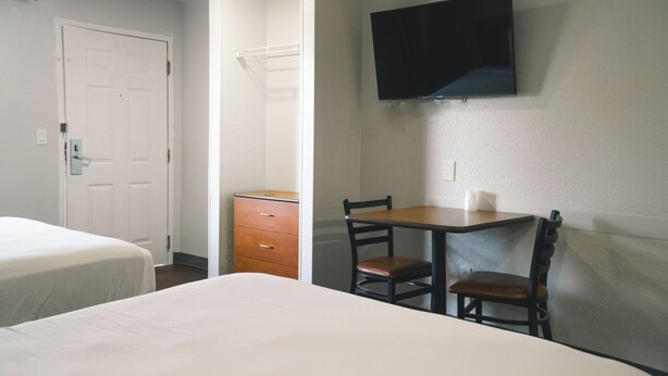 A hotel room with a bed, a dresser, a desk with two chairs, and a flat-screen TV mounted on the wall. - Studio 6 Rancho Cordova, CA (Rancho Cordova)