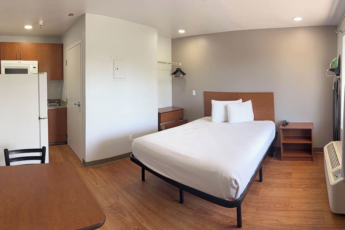 Ein Hotelzimmer mit Bett, Nachttisch, kleinem Schreibtisch, Stuhl, einer Küchenzeile und einem Heizkörper.