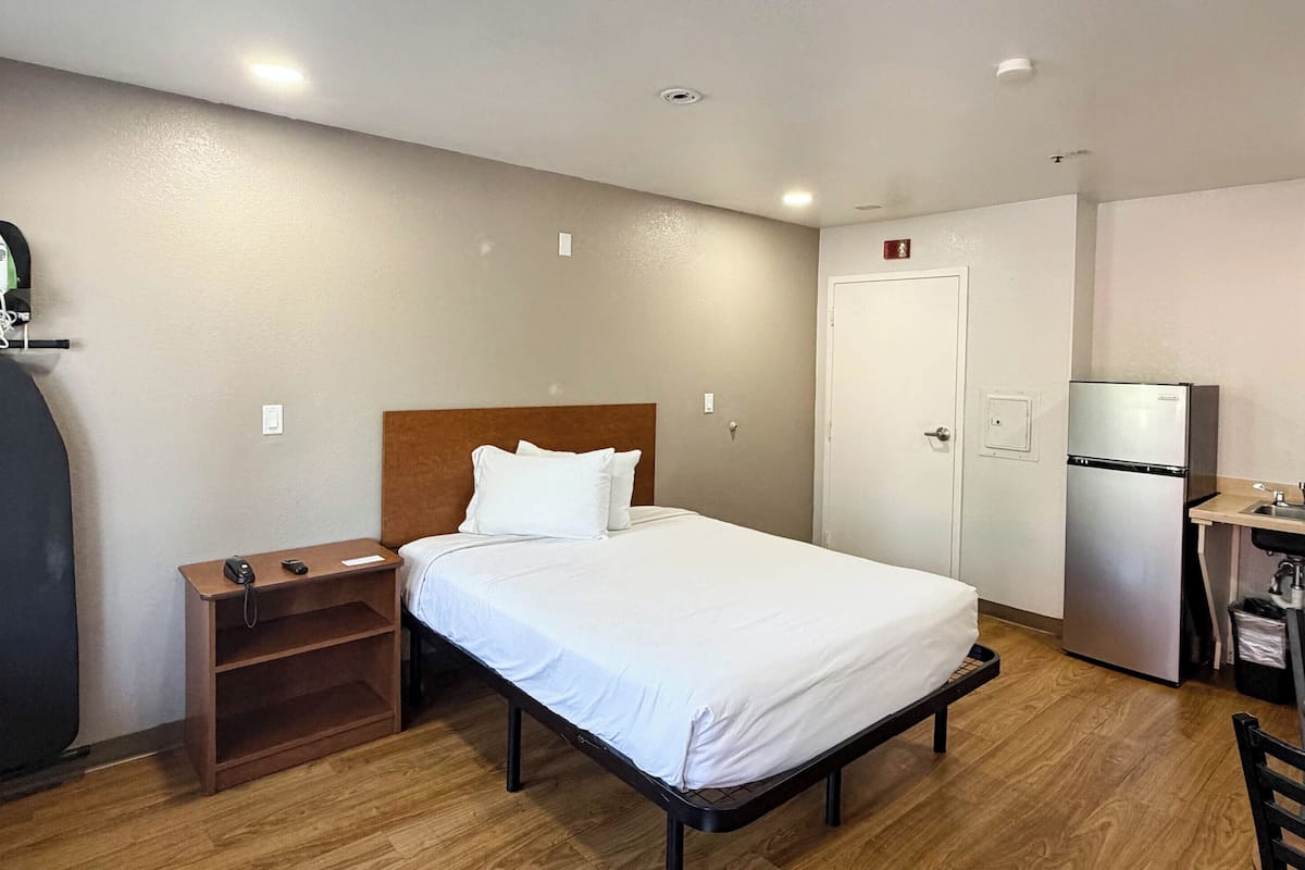Ein Hotelzimmer mit Bett, Schreibtisch, Kühlschrank, Spüle und Kleiderschrank.