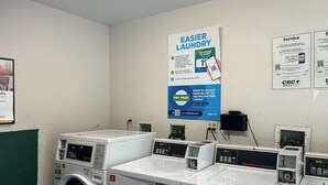 A laundry facility with multiple washing machines and dryers, a sign promoting easier laundry services, and a CSC GO app advertisement. - Studio 6 Rancho Cordova, CA (Rancho Cordova)