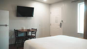 Una habitación de hotel con una cama, un escritorio con dos sillas, un televisor en la pared y una puerta con ventana.