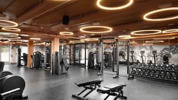 Une salle de sport équipée de matériel d’exercice, de bancs et d’un mur orné d’une fresque florale.