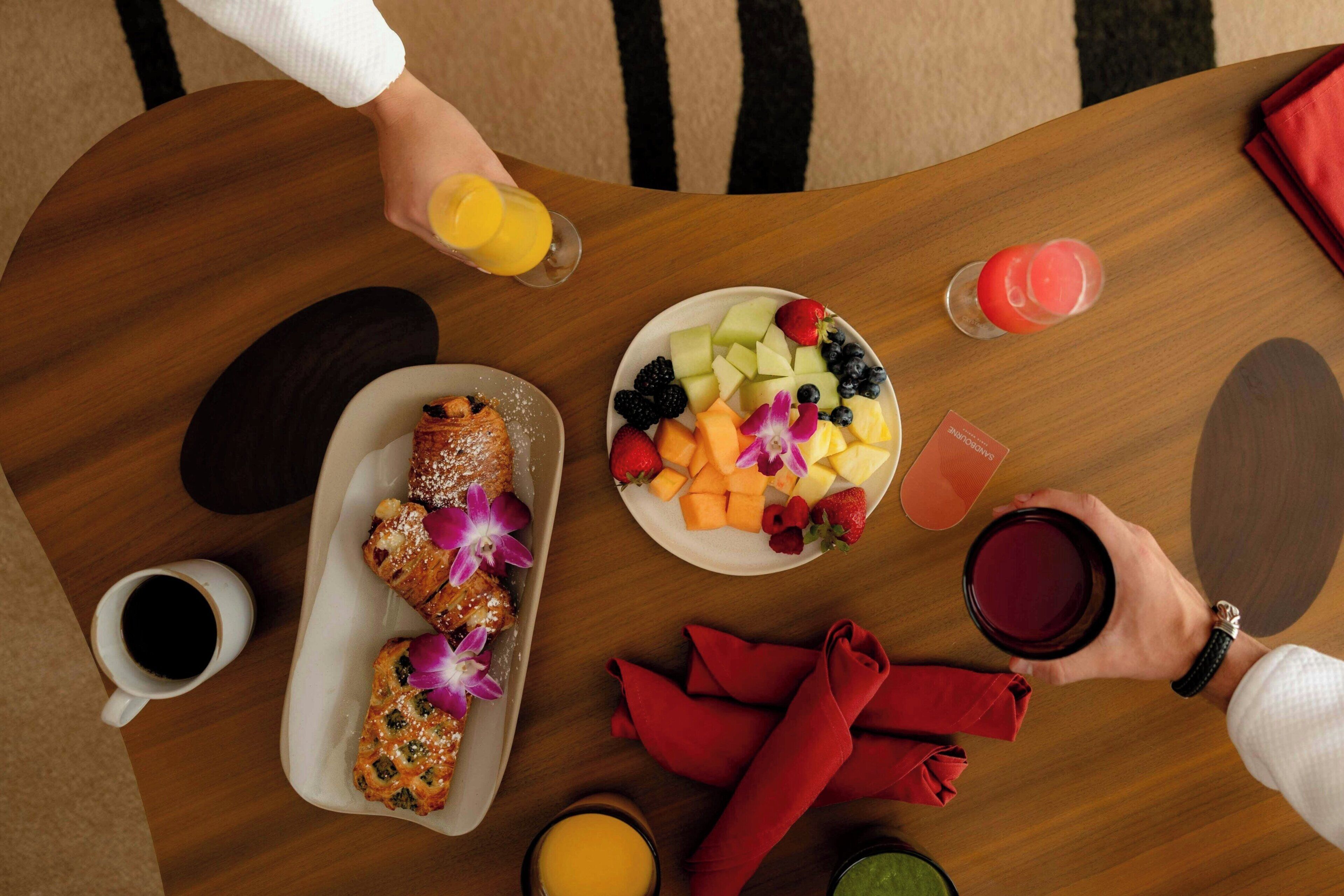 A dining table with a plate of fruit, a pastry, a cup of coffee, and a glass of juice.