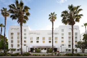 A white hotel with a symmetrical facade, palm trees, and a clear sky.