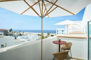 Un balcon avec vue sur la plage et l’océan, comprenant deux fauteuils en osier et une petite table ronde.