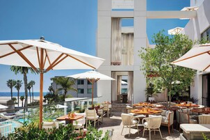 An outdoor patio with tables and chairs, umbrellas, and a view of the ocean.