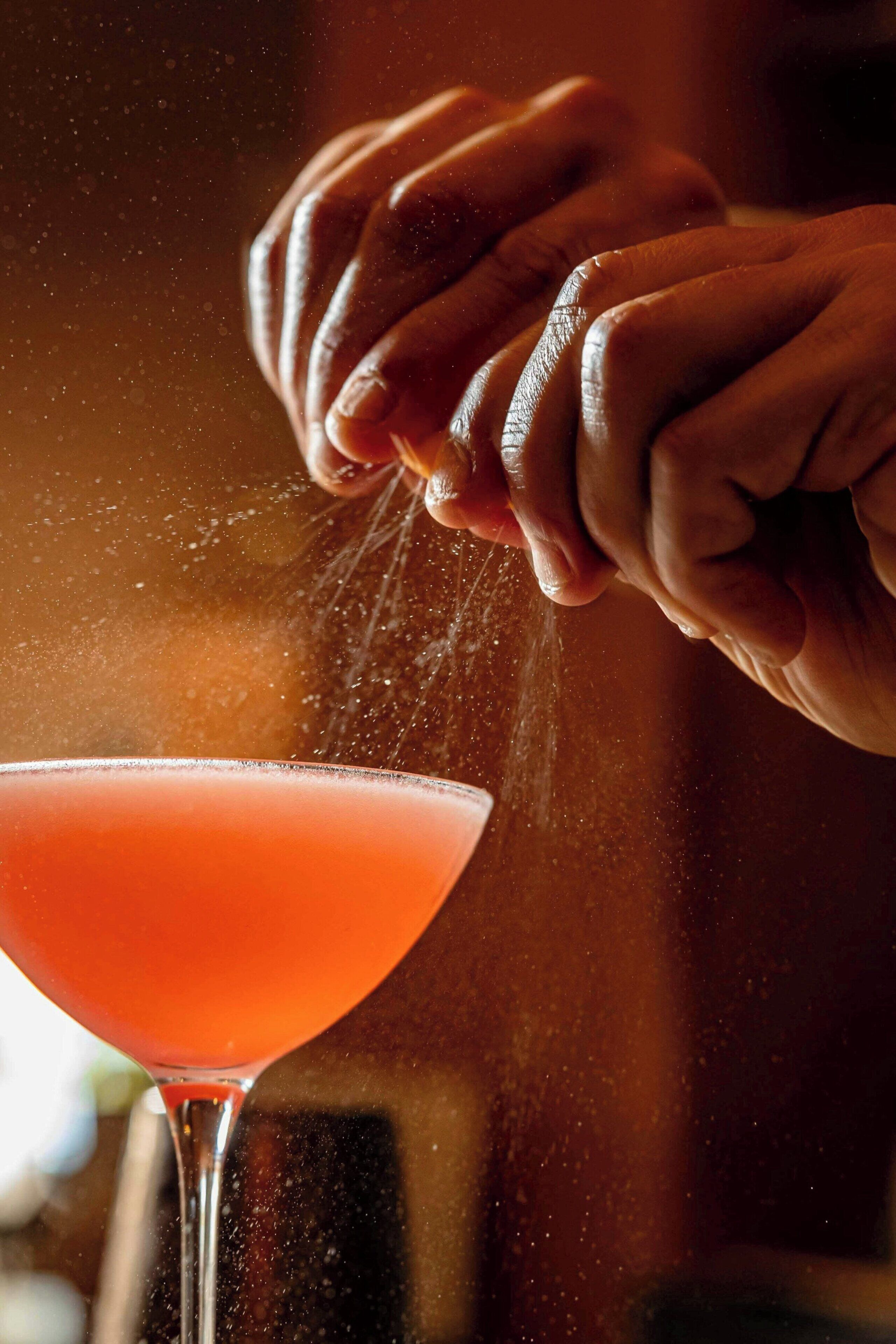 A hand sprinkling a powder onto a drink in a glass.