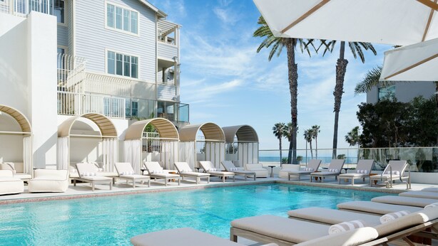 A poolside area with lounge chairs and umbrellas, a clear blue pool, and a building with balconies. - Sandbourne Santa Monica, Autograph Collection (Santa Monica)