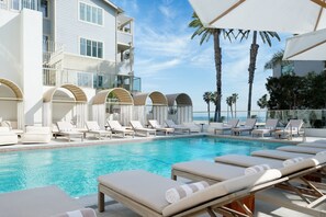 Un espace aménagé au bord de la piscine, avec des chaises longues et des parasols, une piscine à l’eau cristalline et un bâtiment doté de balcons.