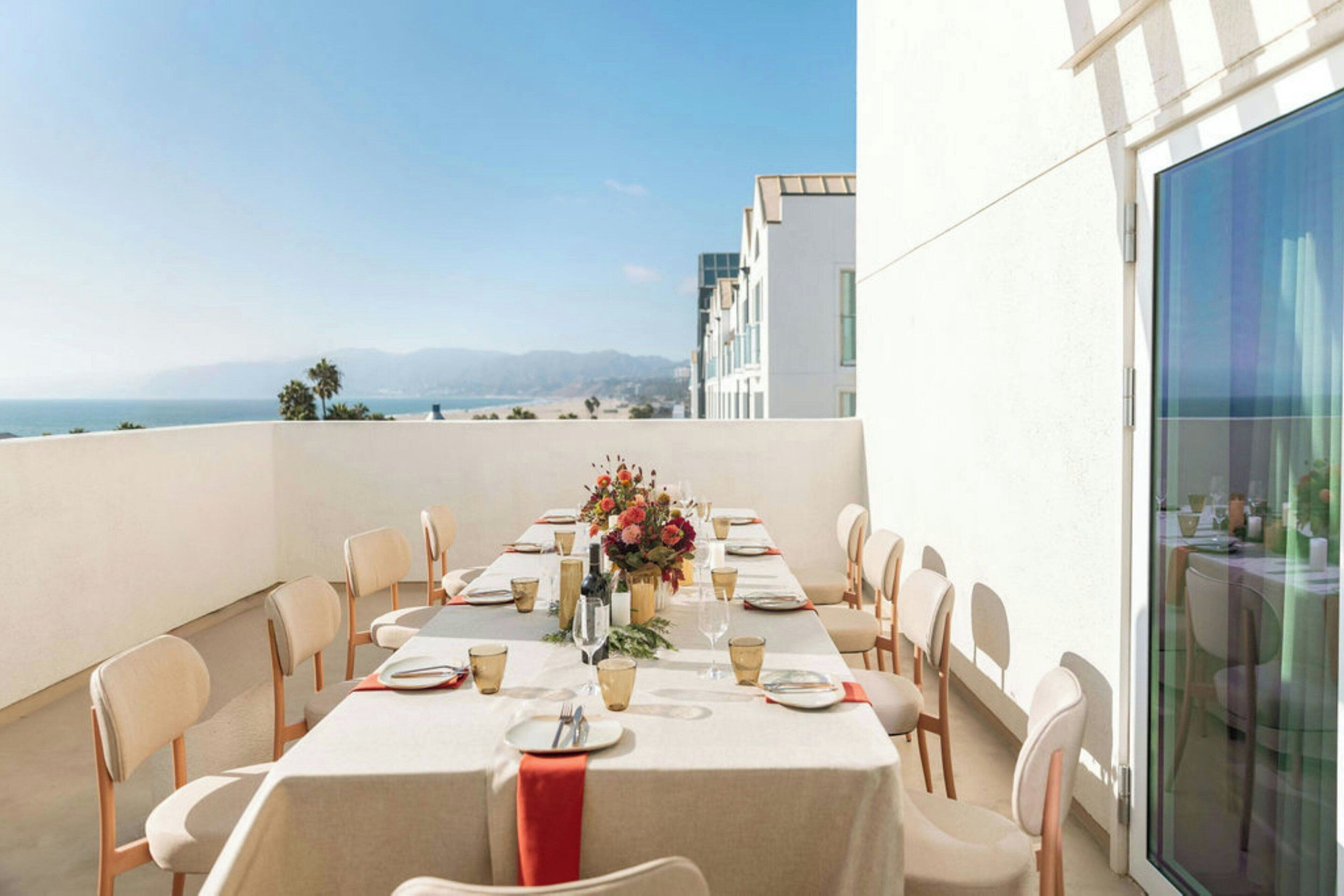 Un coin repas avec une table dressée pour six personnes, offrant une vue panoramique sur l’océan et les montagnes.