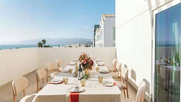 Un coin repas avec une table dressée pour six personnes, offrant une vue panoramique sur l’océan et les montagnes.