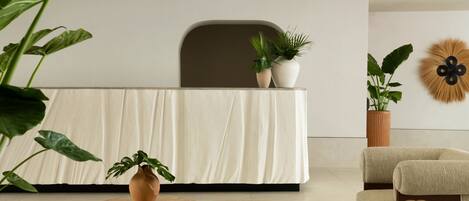 A modern reception area with a neutral color scheme, featuring a reception desk, seating area, and potted plants.