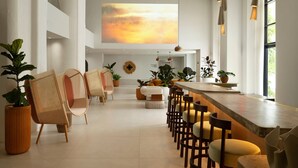 A modern interior with a long bar, wicker chairs, and potted plants. - Sandbourne Santa Monica, Autograph Collection (Santa Monica)