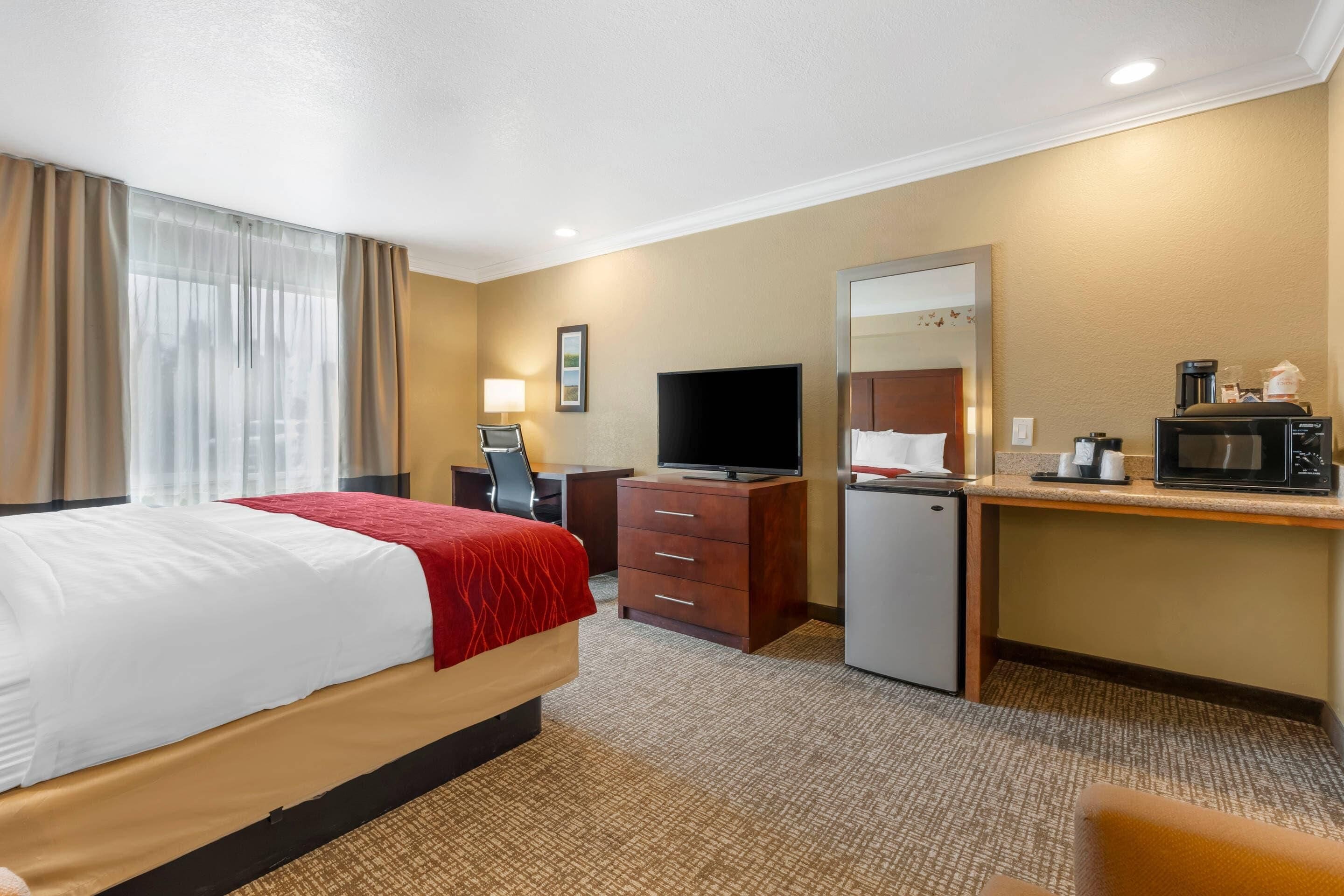 A hotel room with a bed, desk, television, and kitchenette.