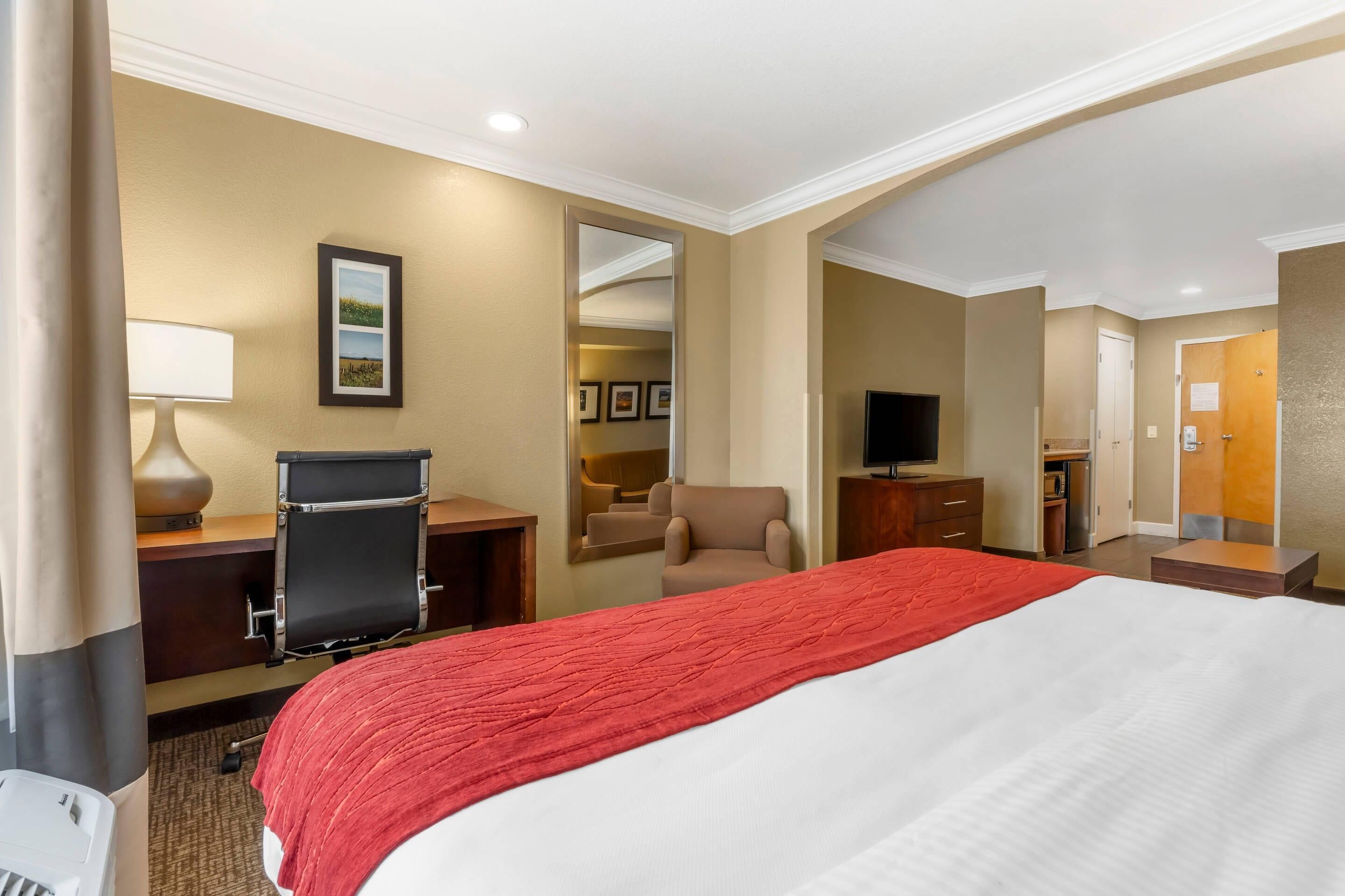 A hotel room with a large bed, a desk with a chair, a TV, and a mirror.