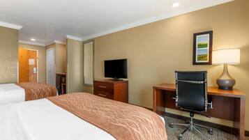 A hotel room with two beds, a desk with a chair, a television, and a lamp.