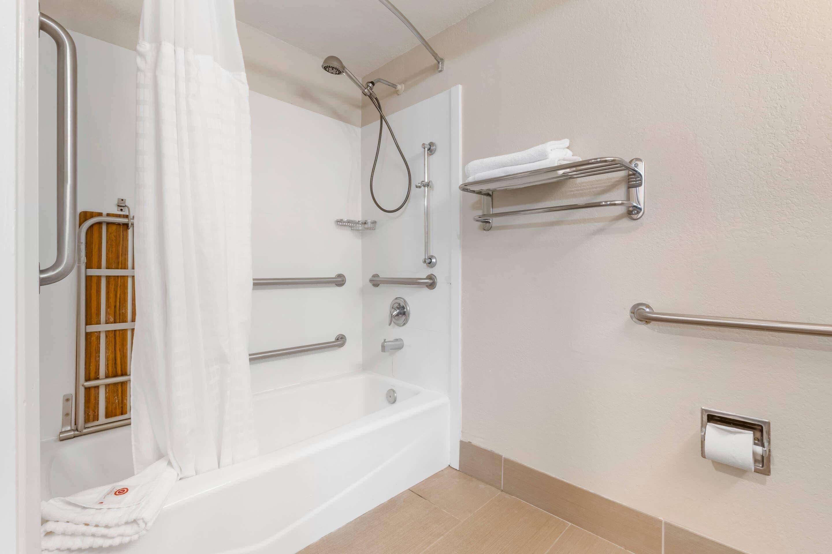 A bathroom with a white bathtub, grab bars, a showerhead, a towel rack, and a toilet paper holder.