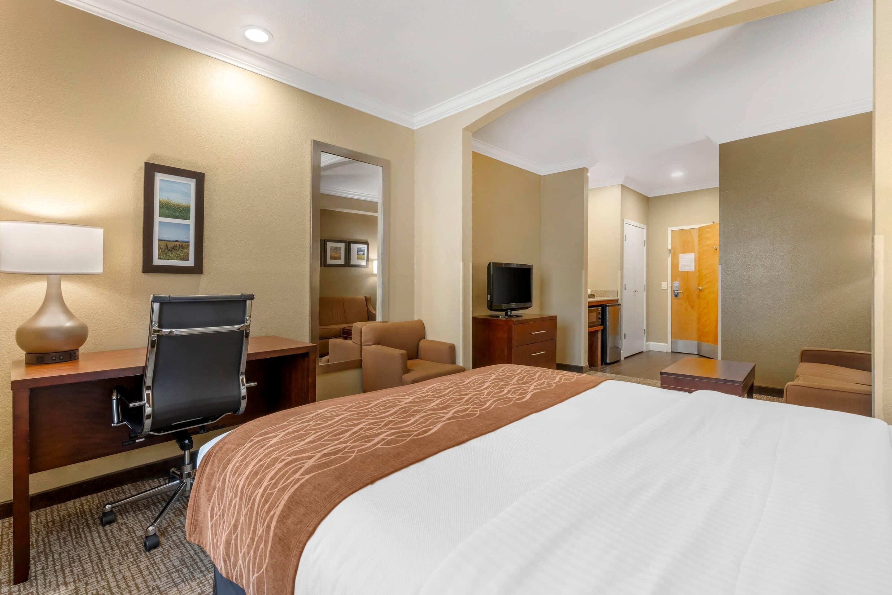 A hotel room with a large bed, a desk with a chair, a television, and a seating area with a sofa and armchairs.