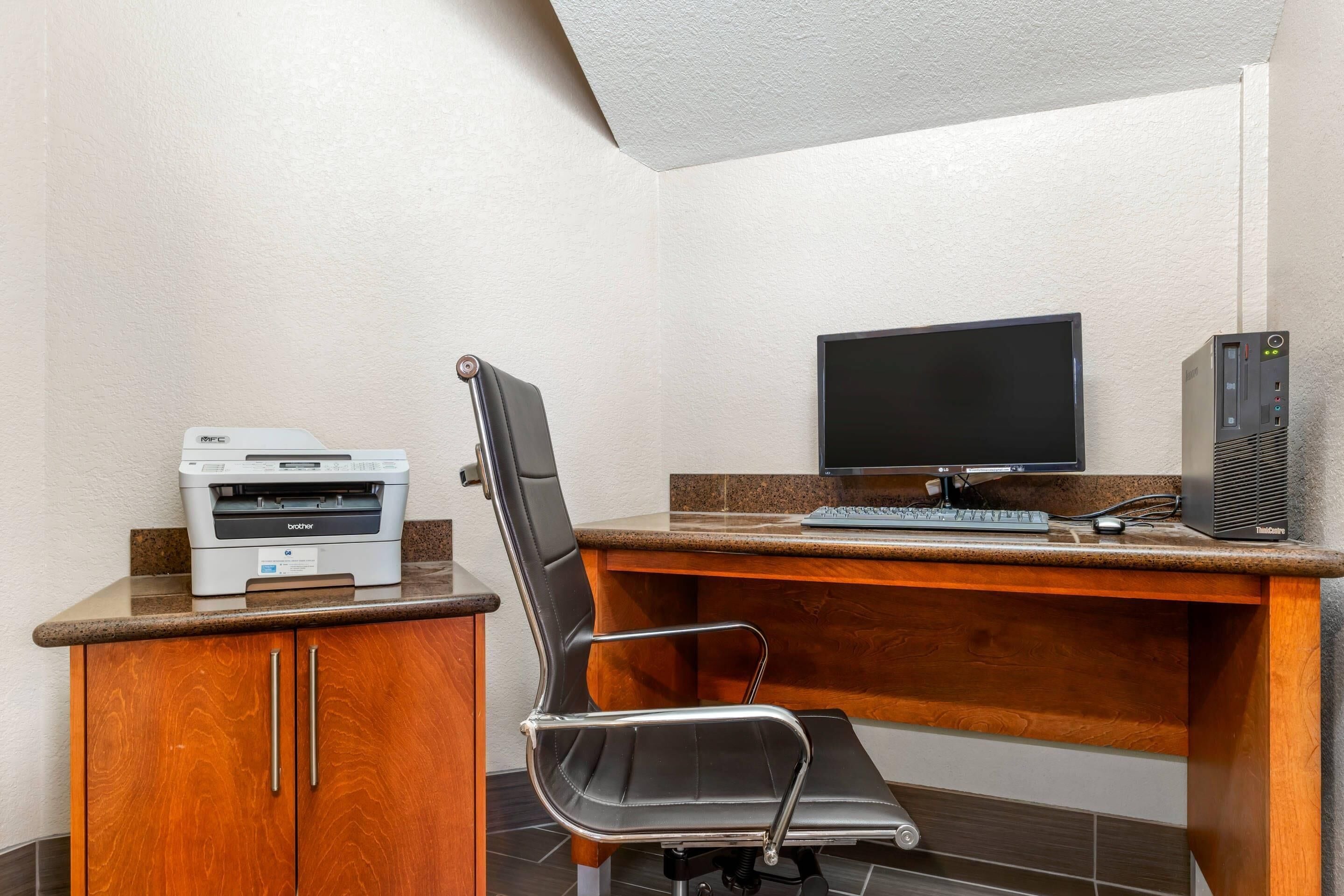 A workspace with a desk, a chair, a printer, a monitor, and a computer tower.
