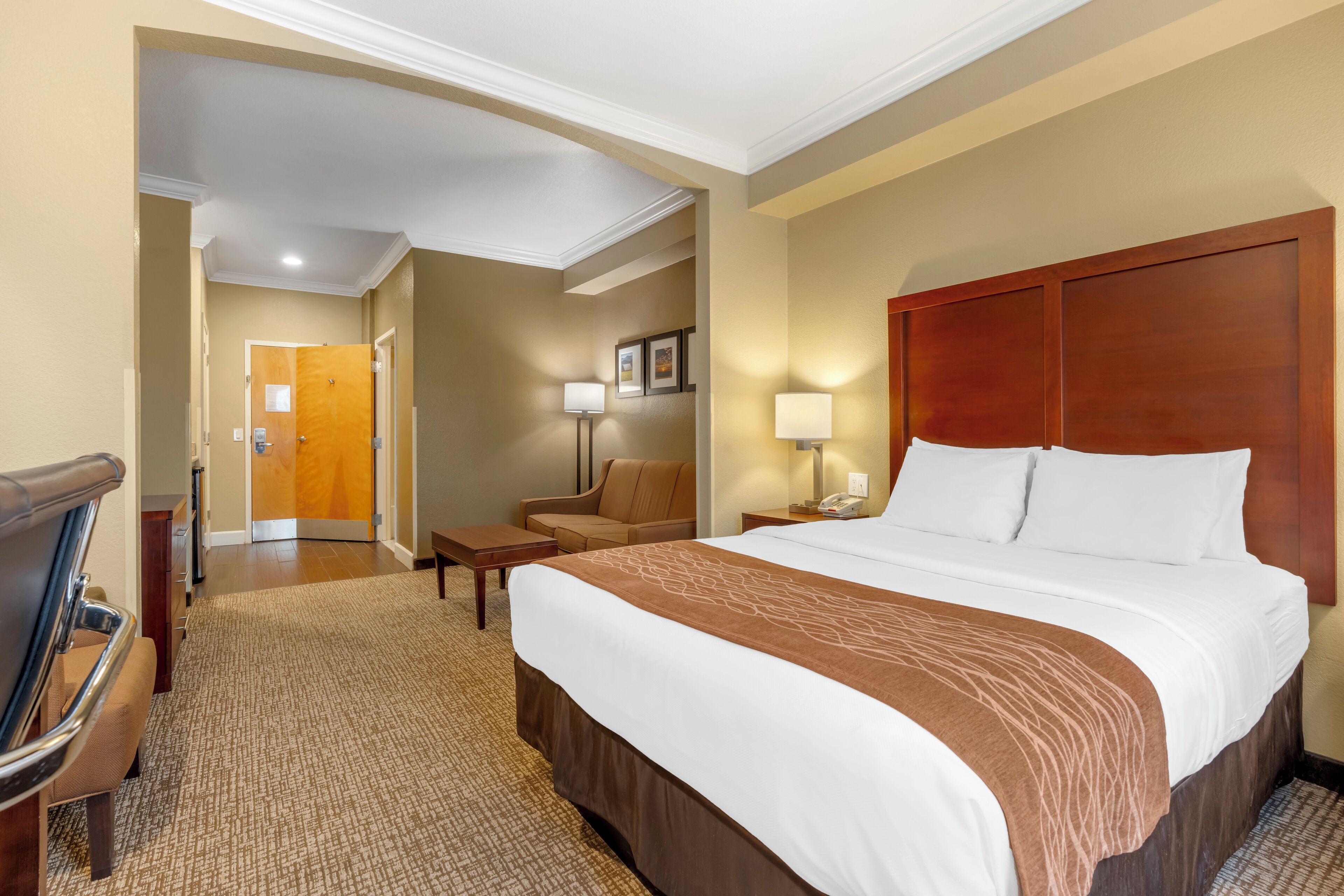 A hotel room with a large bed, a desk, a chair, and a door leading to another room.