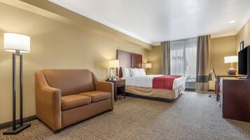 Una habitación de hotel con cama, sofá marrón, escritorio y televisión.