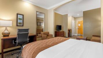 A hotel room with a large bed, a desk with a chair, a television, and a bathroom visible through an open door.