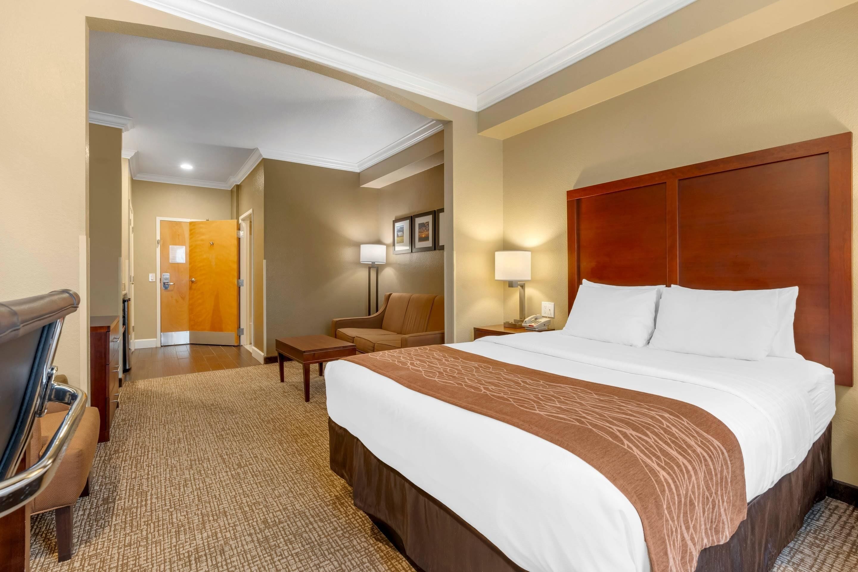 A hotel room with a large bed, a desk, a chair, and a small table.