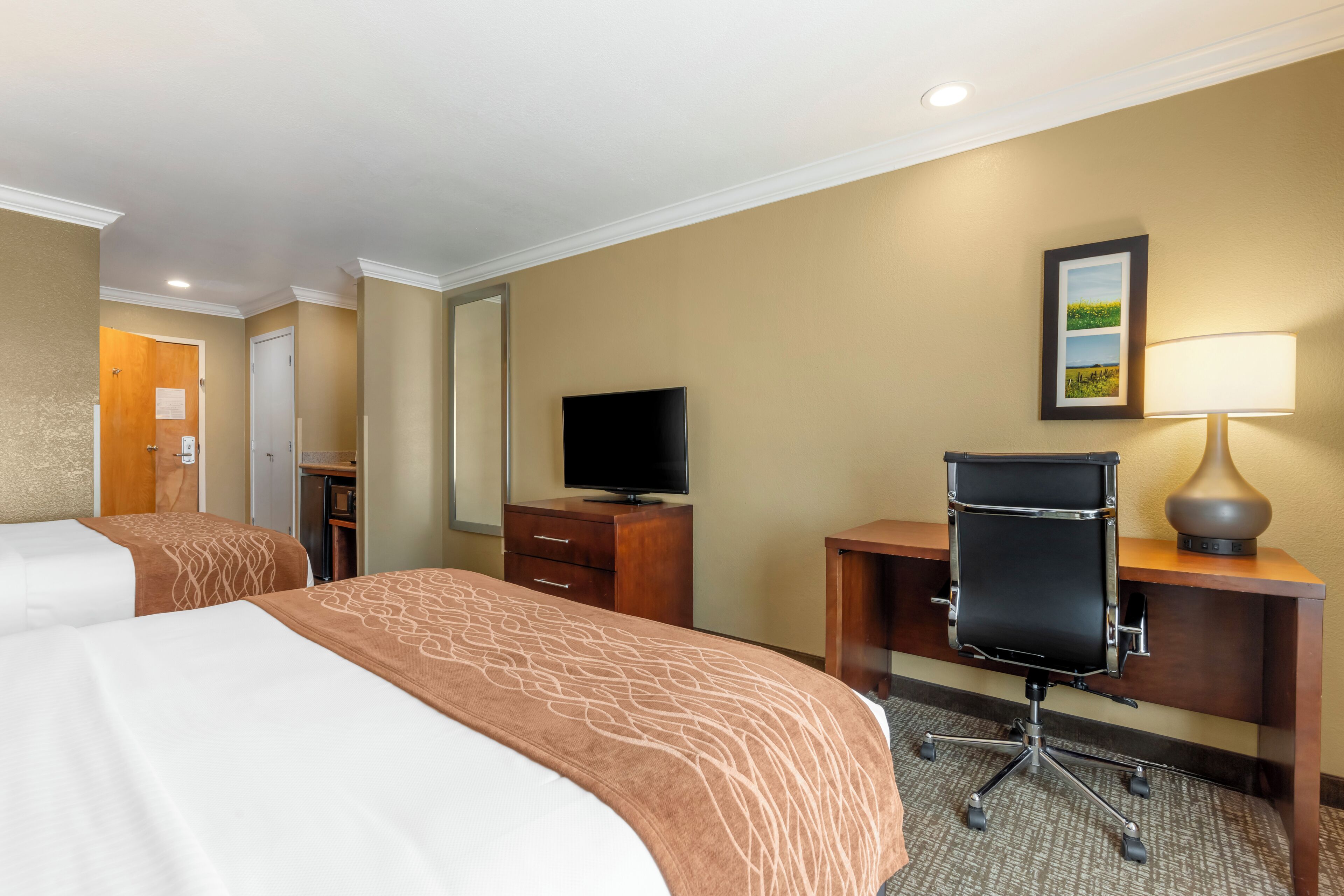 A hotel room with two beds, a desk with a chair, a television, and a lamp.