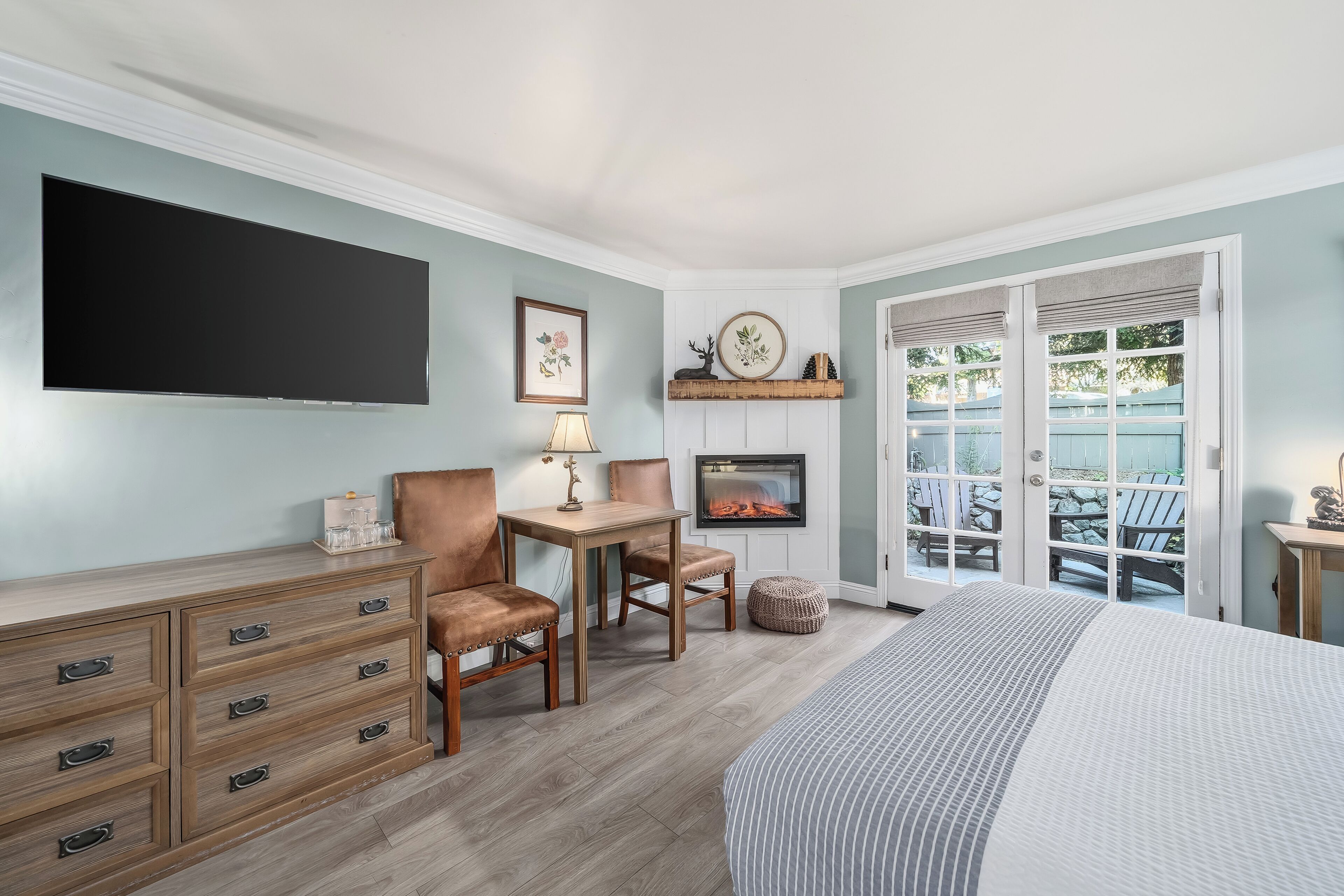 Een slaapkamer met een bed, een kaptafel, een tafel, stoelen, een open haard en uitzicht op buiten.
