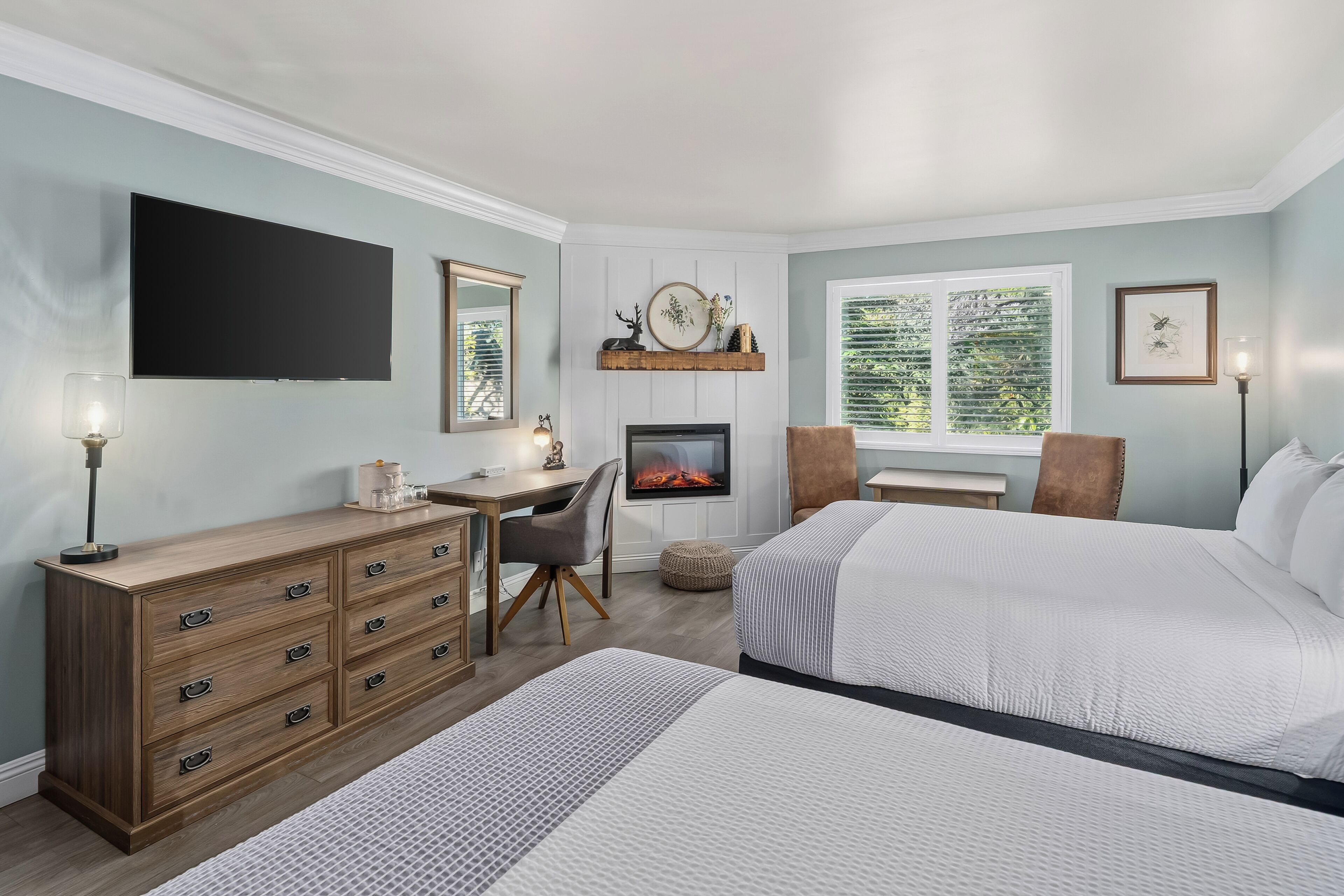 A bedroom with a bed, dresser, desk, chair, fireplace, and a window with blinds.