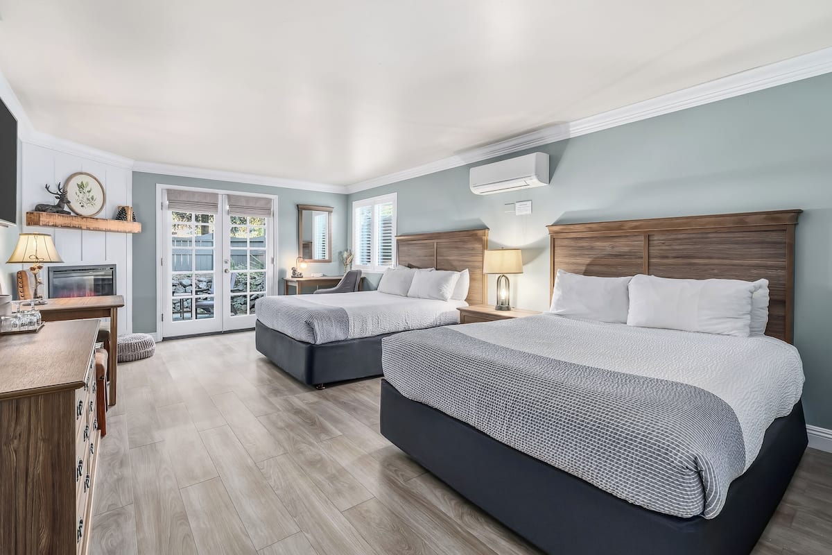 A hotel room with two beds, a desk, a chair, a lamp, a mirror, and a window with blinds.