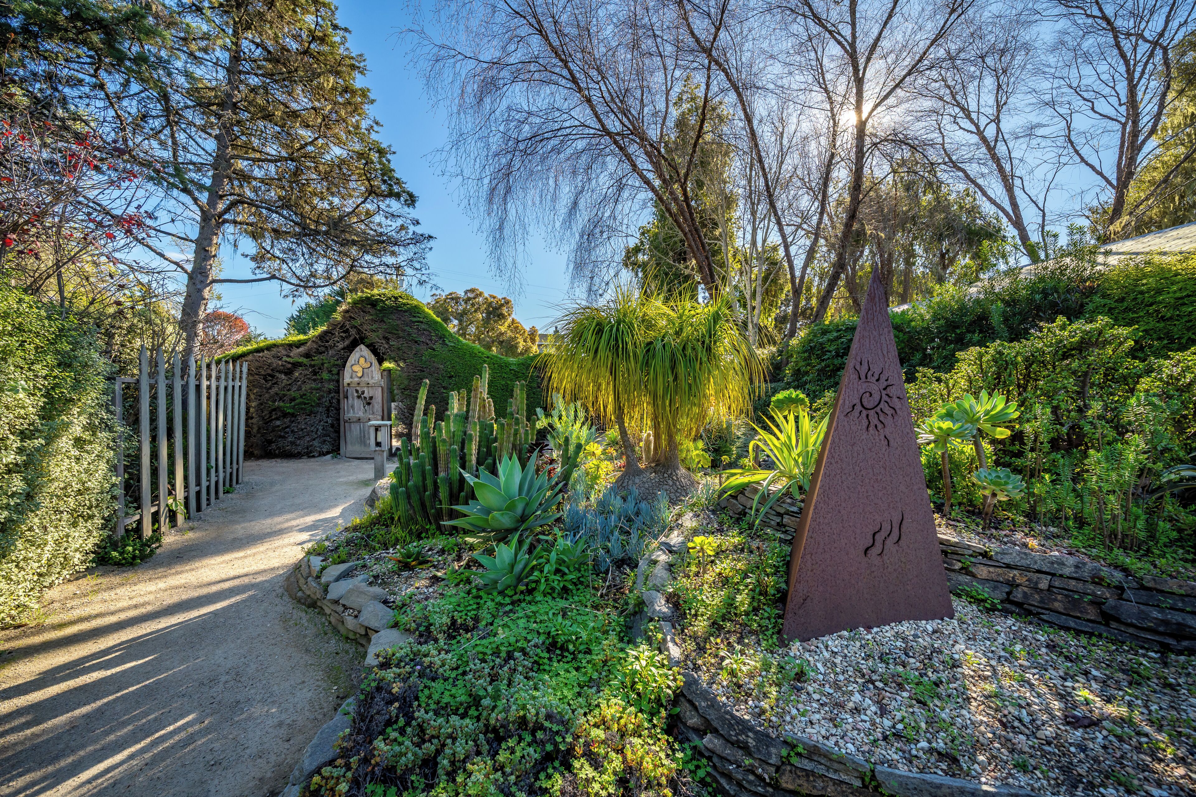 A garden pathway leading to a gazebo, surrounded by various plants and a stone wall.