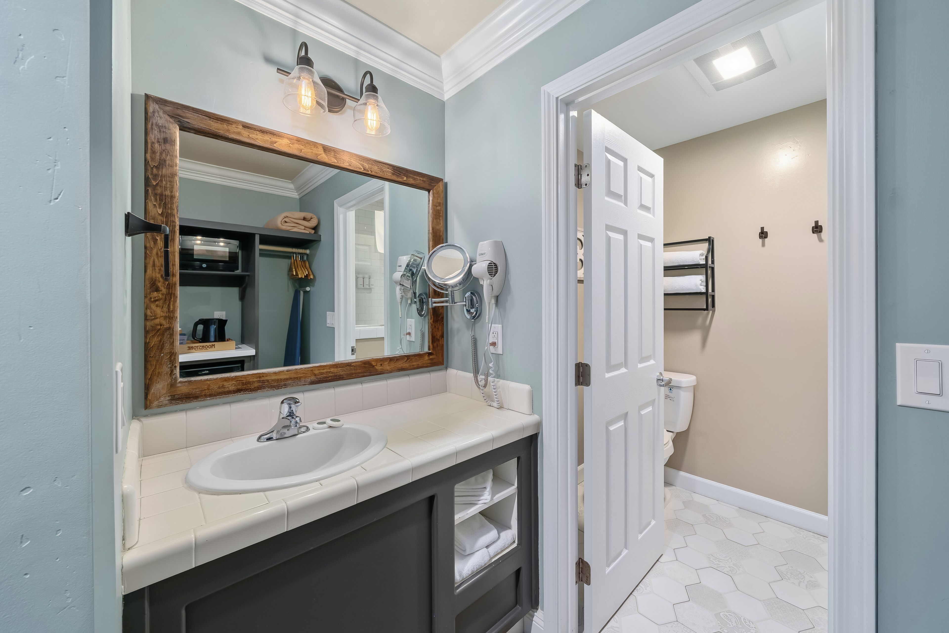 A bathroom with a large mirror, a sink, a towel rack, and a toilet.