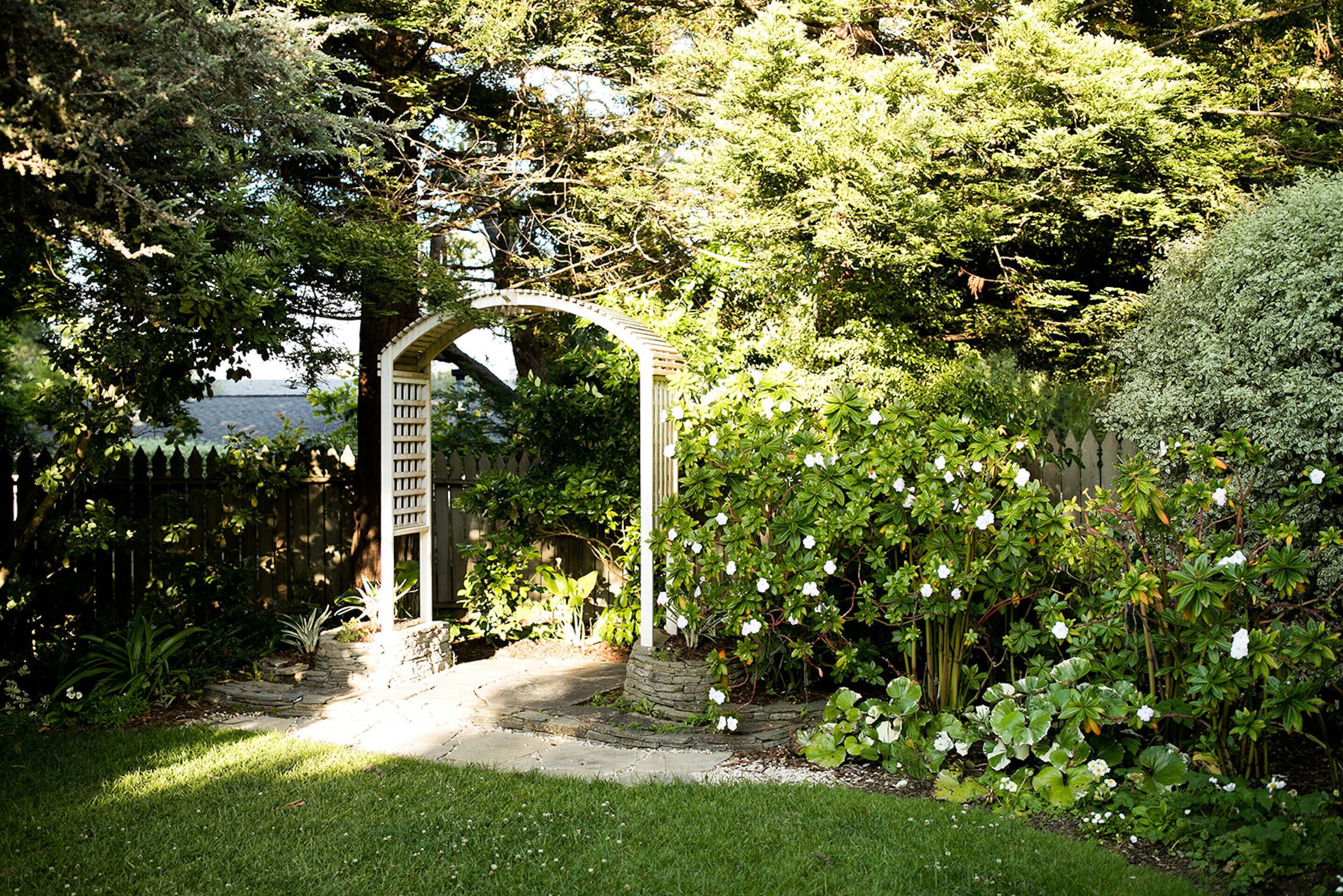 A garden with a white arbor and a stone pathway leading to it.