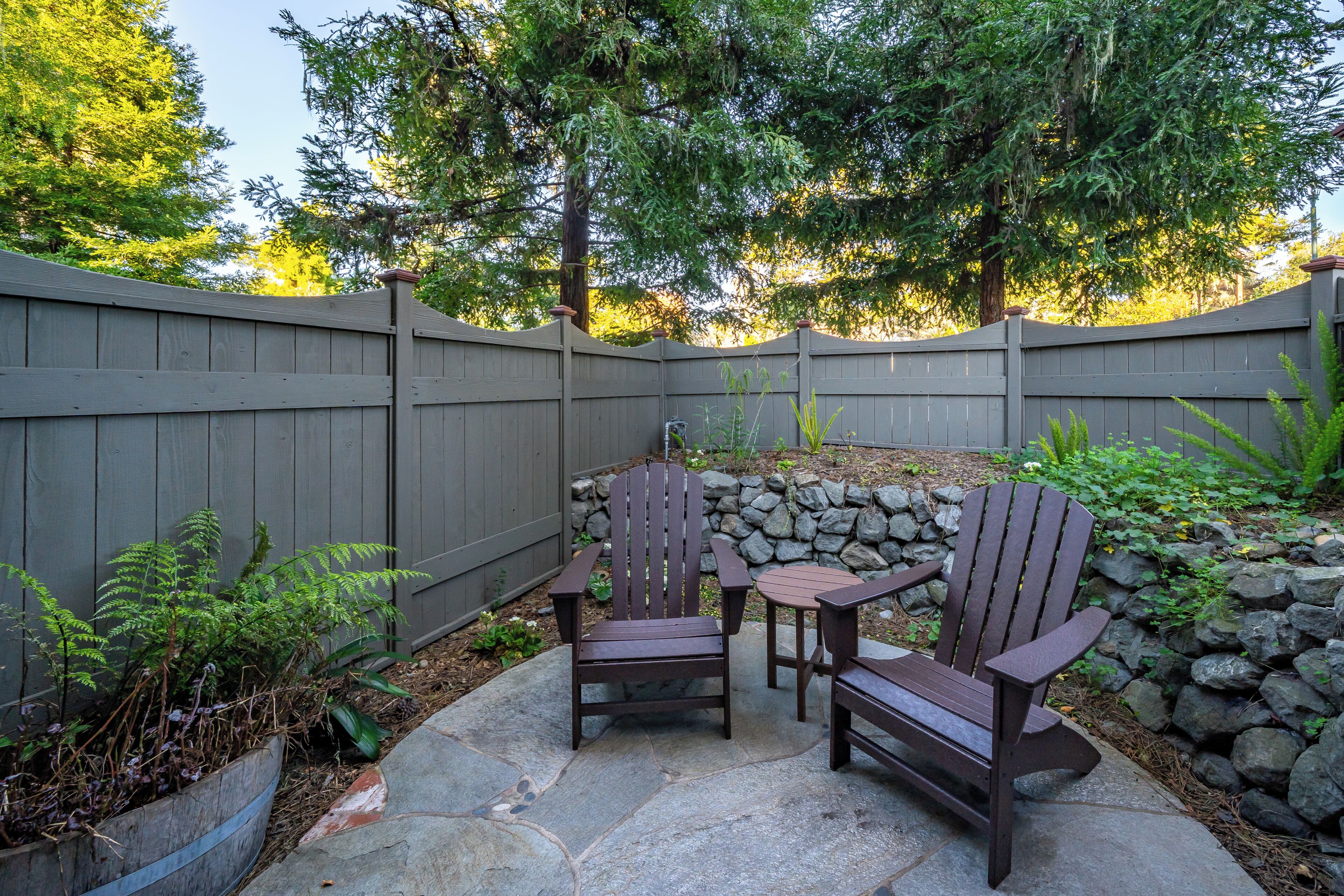 A patio with Adirondack chairs, a stone table, and a wooden fence.
