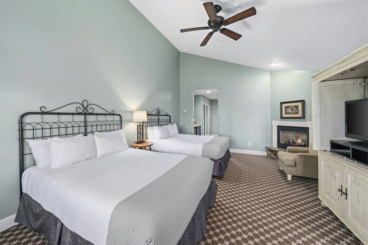 A bedroom with two beds, a ceiling fan, a fireplace, a TV, and a patterned carpet.