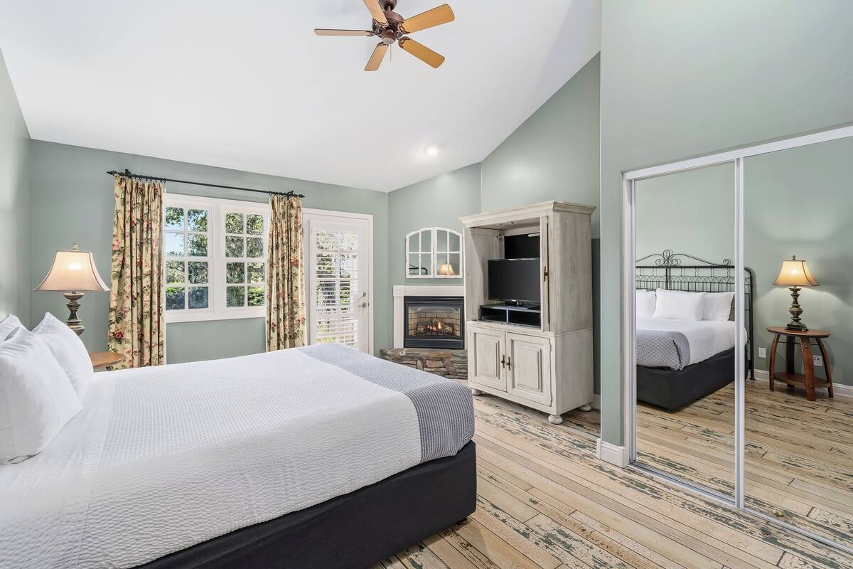 A bedroom with a bed, a television, a fireplace, a wardrobe, and a mirror.