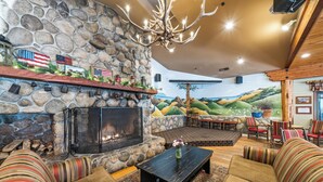 A stone fireplace with American flags, a chandelier, and a mural of a landscape. - Cambria Pines Lodge (Cambria)
