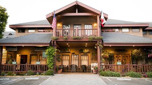 A two-story building with a balcony, outdoor seating, and flags. - Cambria Pines Lodge (Cambria)